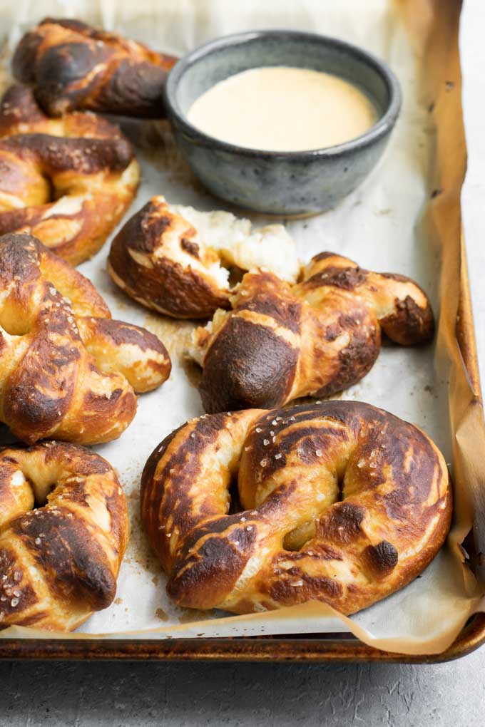 homemade soft pretzels on a baking tray with a mustard beer dip for dipping in the background