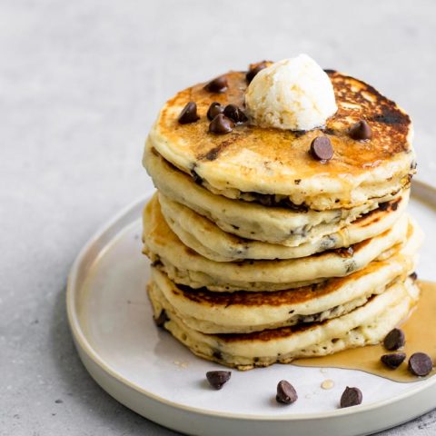 a stack of vegan chocolate chip panckes topped with vegan butter, chocolate chips, and maple syrup