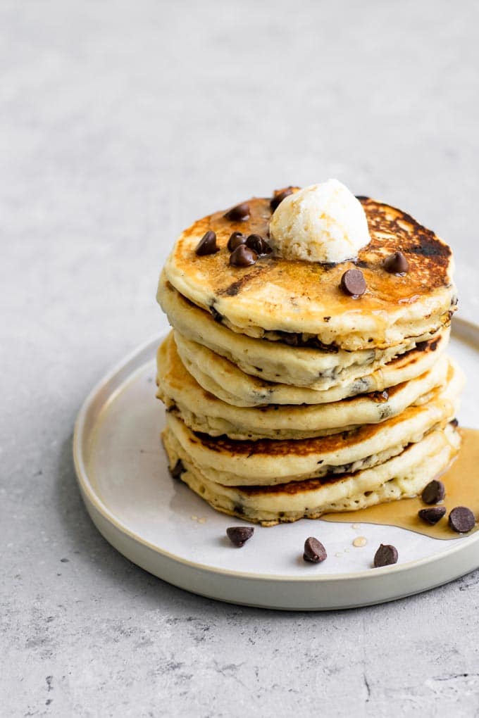 a stack of vegan chocolate chip panckes topped with vegan butter, chocolate chips, and maple syrup