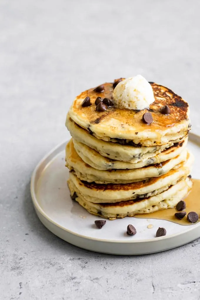 a stack of vegan chocolate chip panckes topped with vegan butter, chocolate chips, and maple syrup