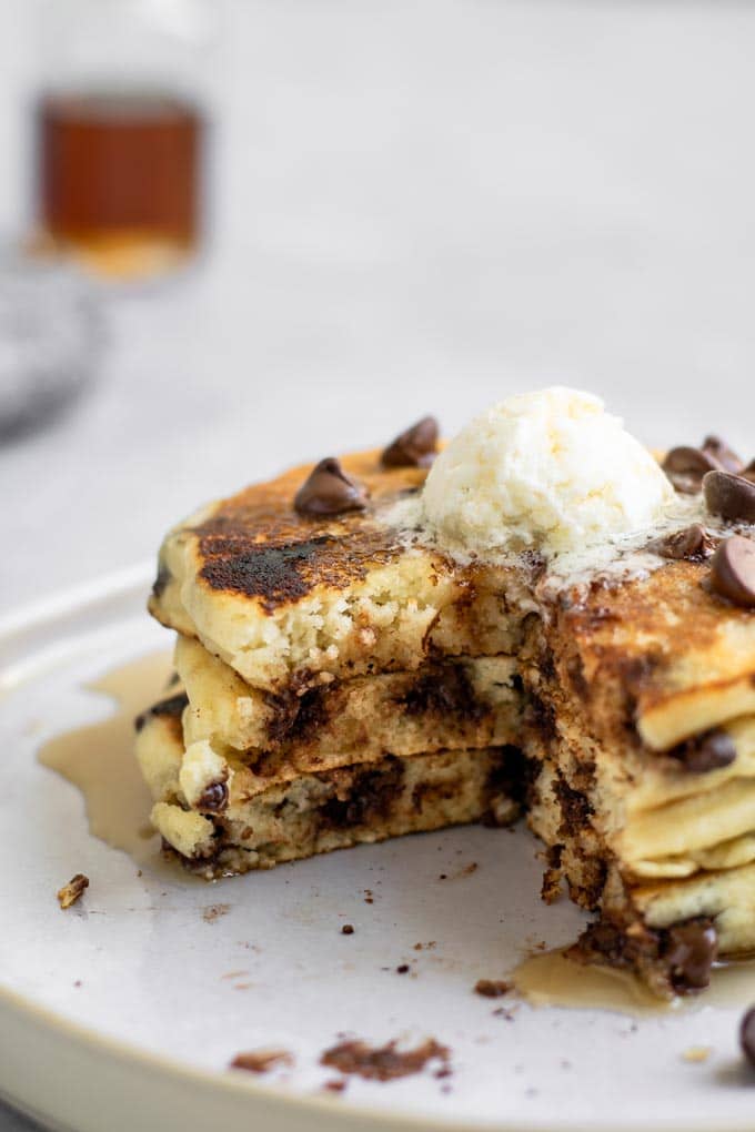 3 vegan chocolate chip pancakes stacked and topped with vegan butter, with a wedge cut out to show the inside texture of the fluffy pancakes