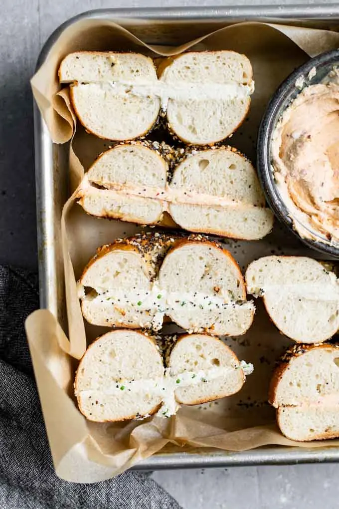 bagels filled with homemade cultured cashew cream cheese, chipotle, chive, and plain flavors. They're cut in half and placed in a parchment lined baking dish with extra chipotle cream cheese