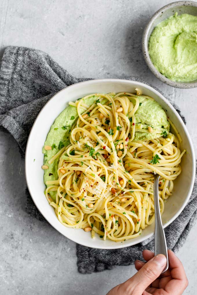 garlic linguine on a bed of vegan whipped pea ricotta overhead shot with a hand twirling pasta on a fork