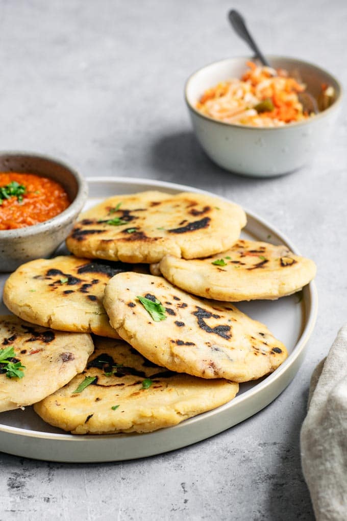 homemade pupusas on a plate, garnished with cilantro and served with a side of curtido and salsa roja