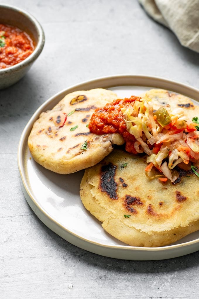 three pupusas on a plate topped with curtido and salsa roja