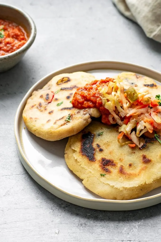 three pupusas on a plate topped with curtido and salsa roja