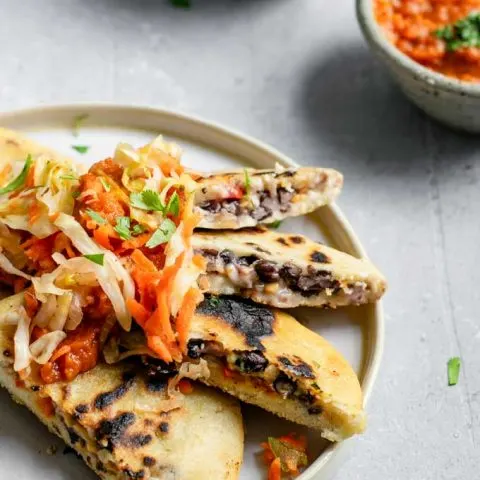 pupusas cut open and fanned on a plate to show the inside filling and texture. Topped with some curtido and salsa roja to serve.