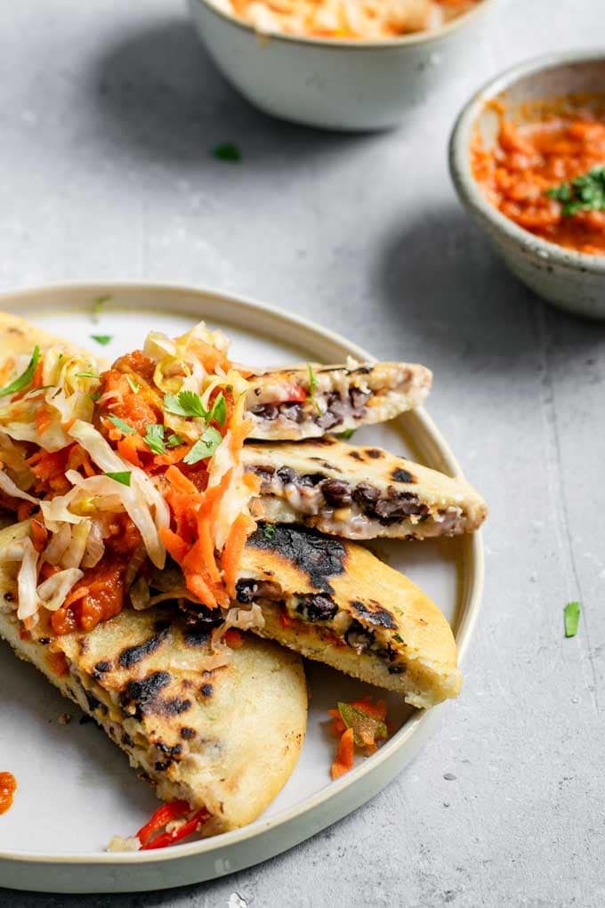 pupusas cut open and fanned on a plate to show the inside filling and texture. Topped with some curtido and salsa roja to serve.