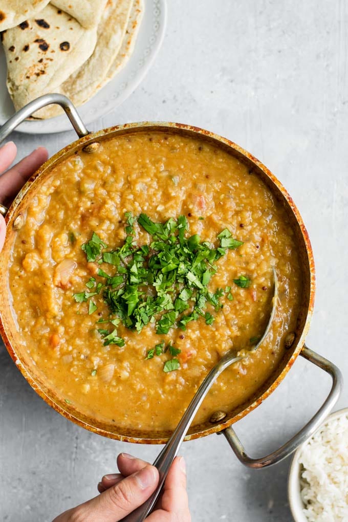 hands spooning red lentil dal tadka to serve with basmati rice and chapati