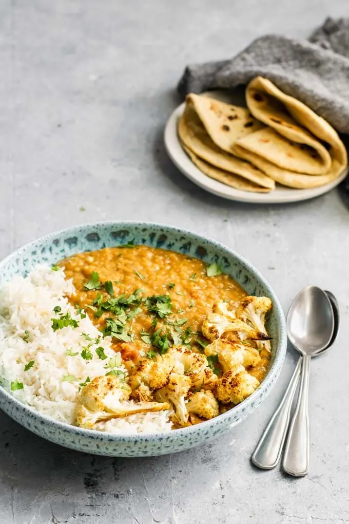 a bowl of masoor dal tadka with basmati rice and roasted cauliflower, served with chapati