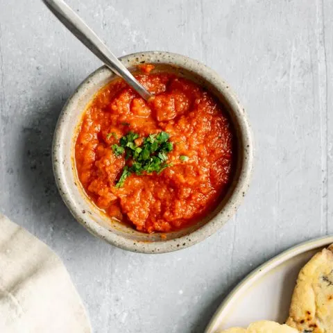 salvadoran salsa roja in a bowl, garnished with cilantro and served with pupusas on a plate on the side