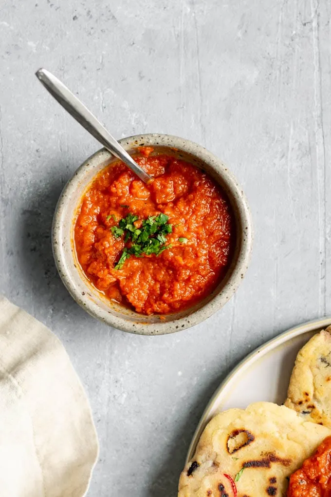 salvadoran salsa roja in a bowl, garnished with cilantro and served with pupusas on a plate on the side