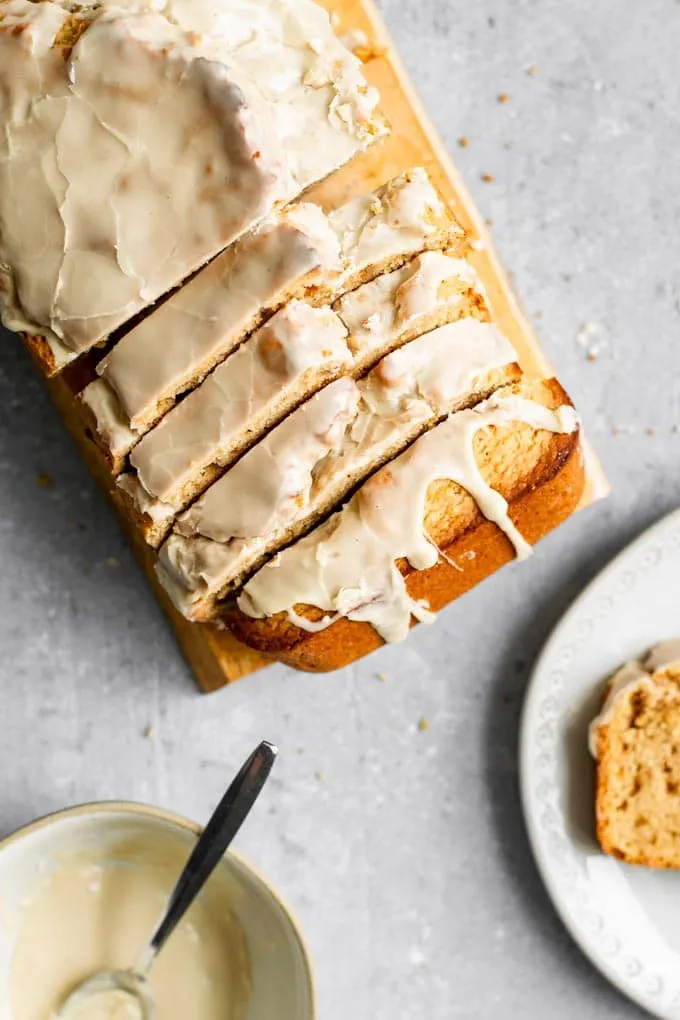 overhead view of sliced chai spice loaf cake with a bowl of glaze and a slice on a plate