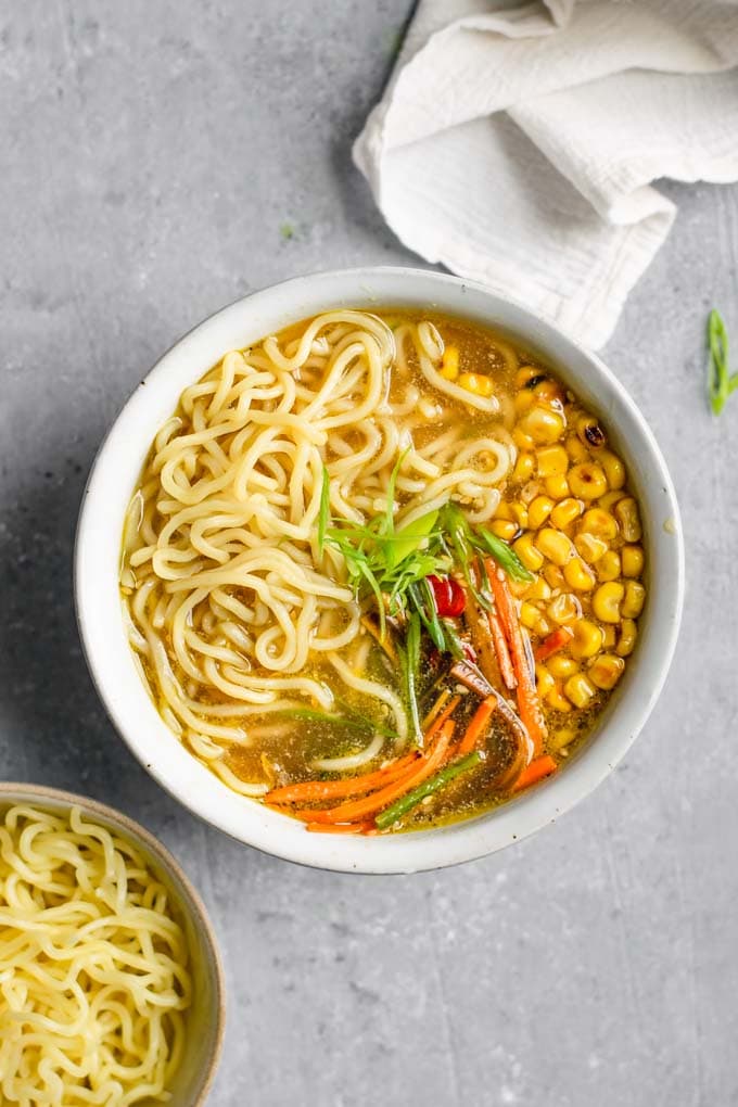 overhead shot of a bowl of vegan ramen with miso tahini broth and an extra bowl of ramen noodles on the side