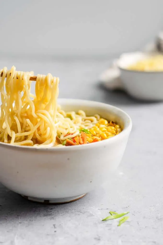 angled view of a bowl of ramen, with the noodles being lifted on chopsticks above the bowl