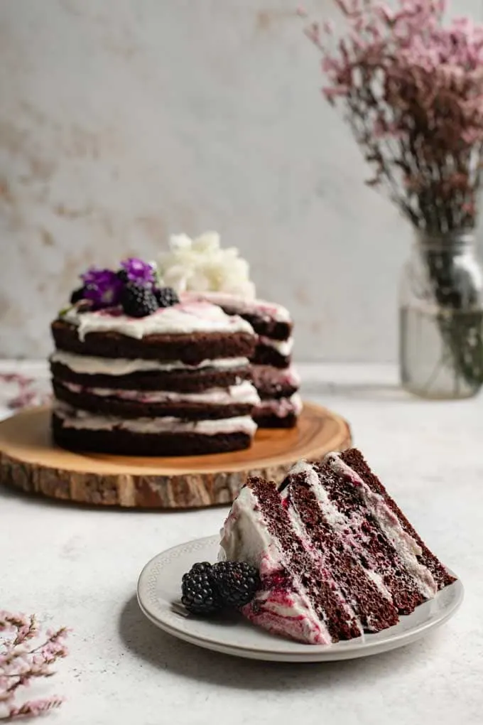 slice of blackberry lavender chocolate cake with the whole cake in the background