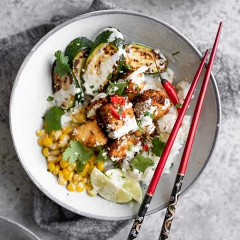crispy coconut tofu poke bowl with wasabi sauce drizzled overtop and red chopsticks