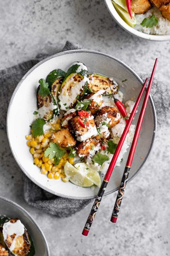 crispy coconut tofu poke bowl with wasabi sauce drizzled overtop and red chopsticks