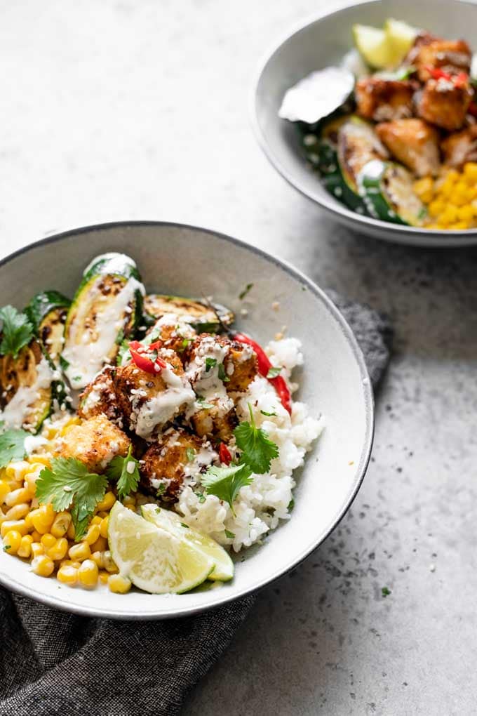 angled view of a a crispy coconut tofu poke bowl with wasabi sauce, sushi rice, zucchini, and corn