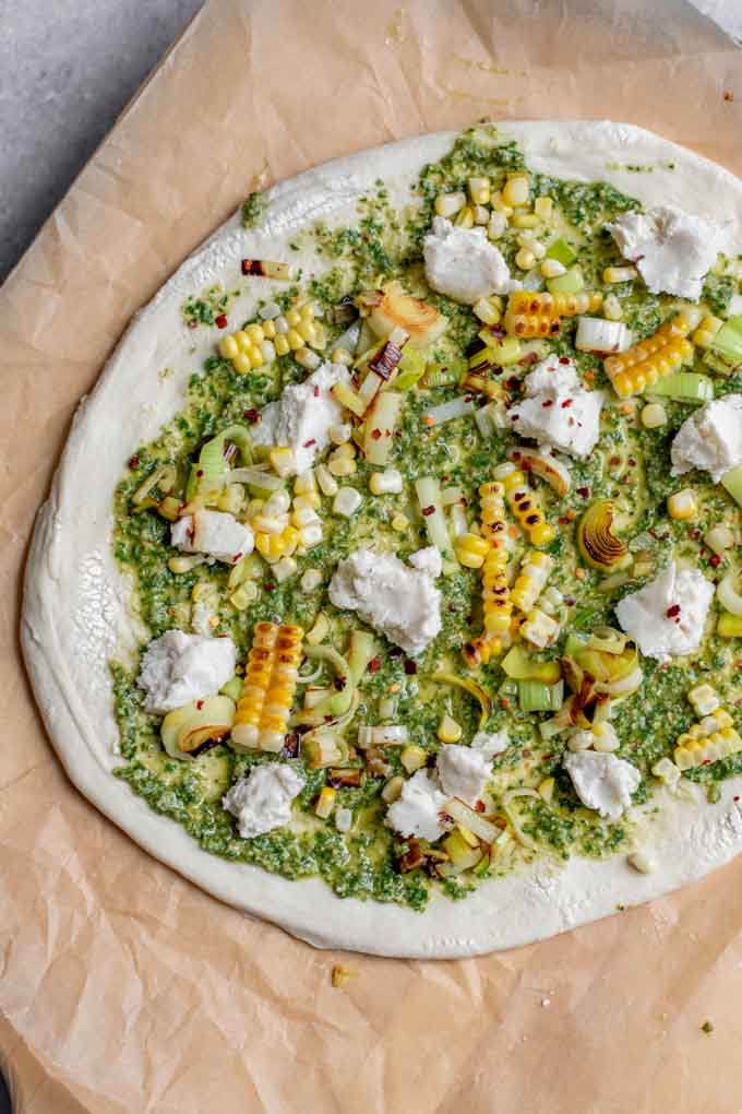 pizza dough spread with pesto, charred leeks, charred corn, and vegan mozzarella.