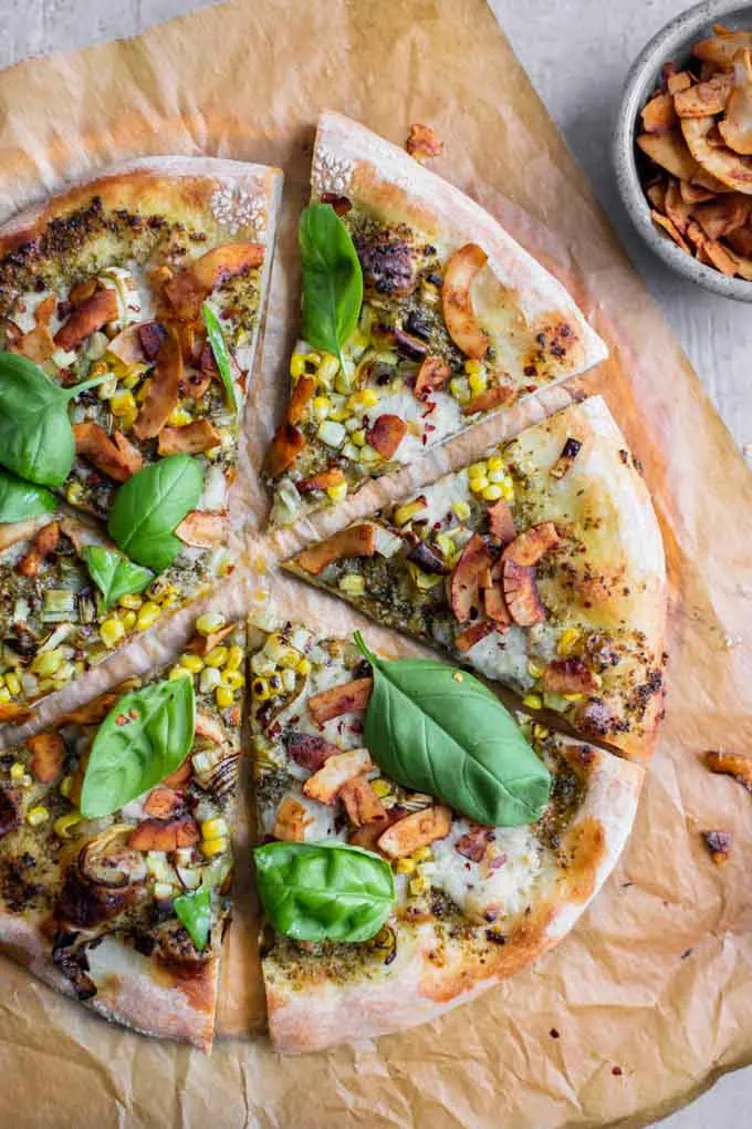 overhead view of sliced pesto leek pizza with coconut bacon on parchment paper