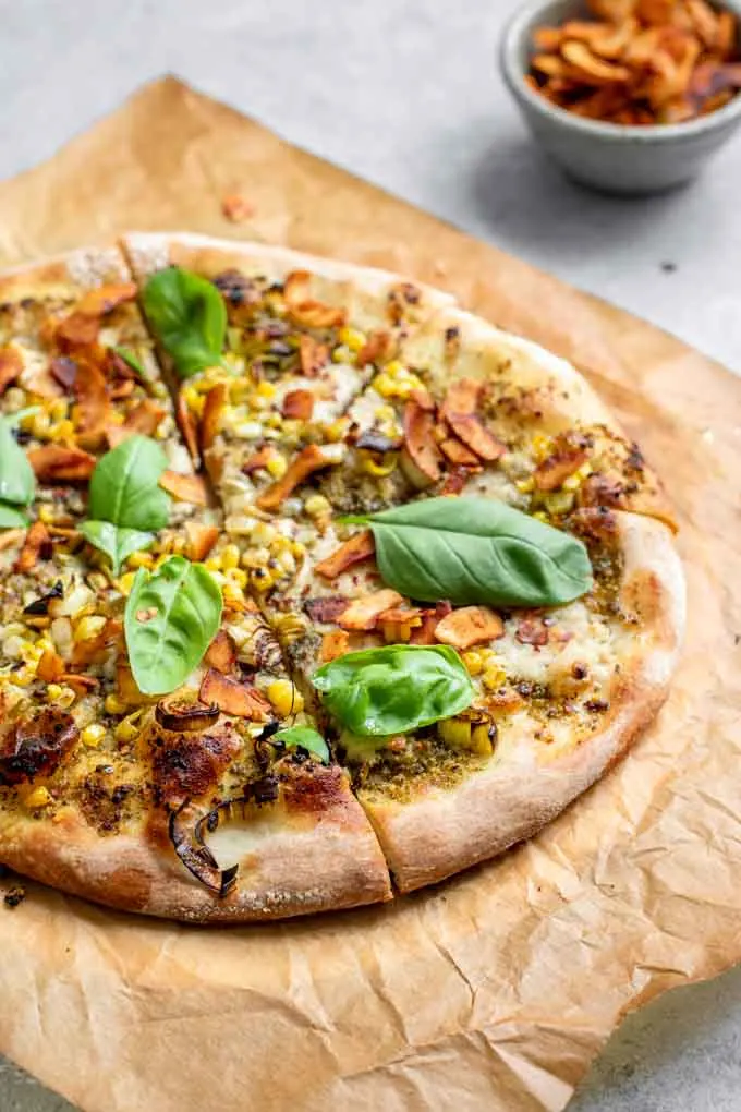 side view of pesto leek pizza sliced and on a piece of parchment paper