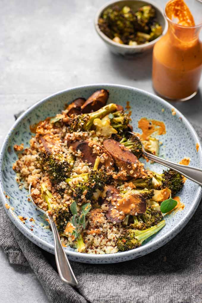 A bowl of roasted broccoli, quinoa, and vegan sausage tossed with roasted red pepper sauce