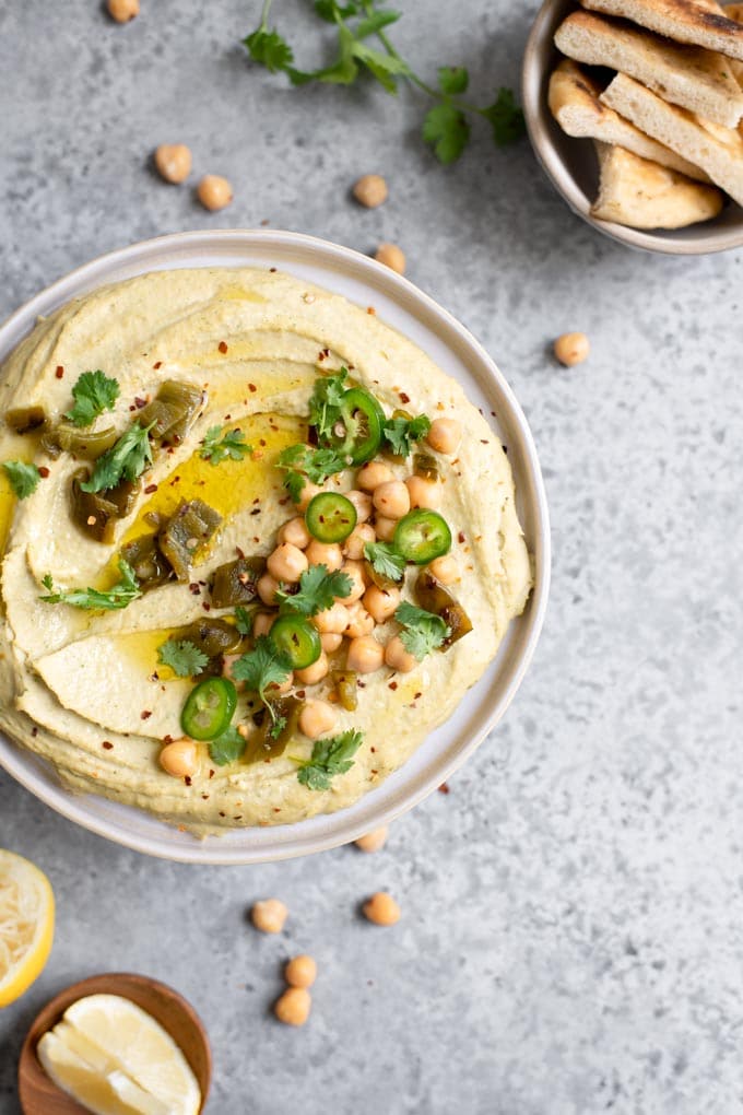 overhead view of roasted jalapeño and cilantro hummus topped with garnishes and extra virgin olive oil