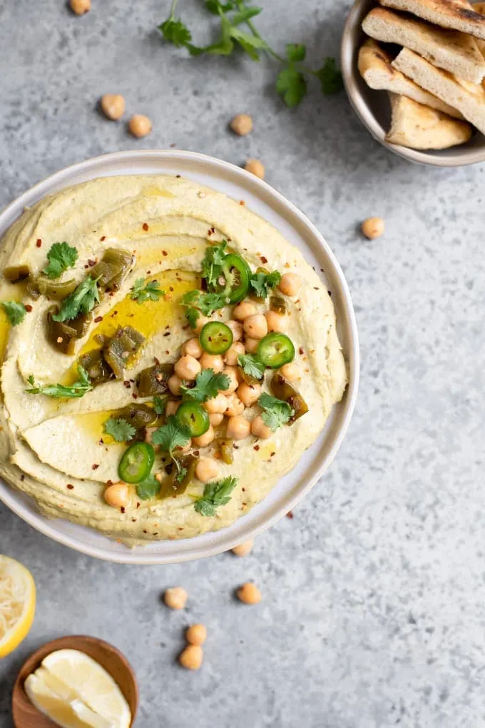 overhead view of roasted jalapeÃ±o and cilantro hummus topped with garnishes and extra virgin olive oil