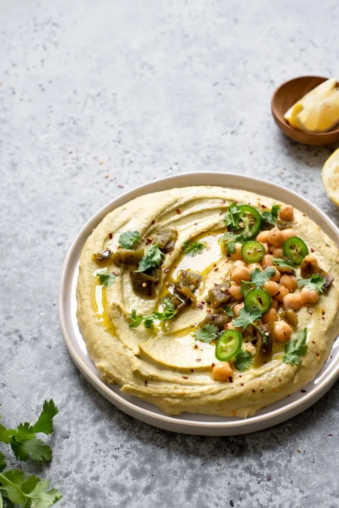 back lit side view of roasted jalapeÃ±o and cilantro hummus topped with garnishes and extra virgin olive oil