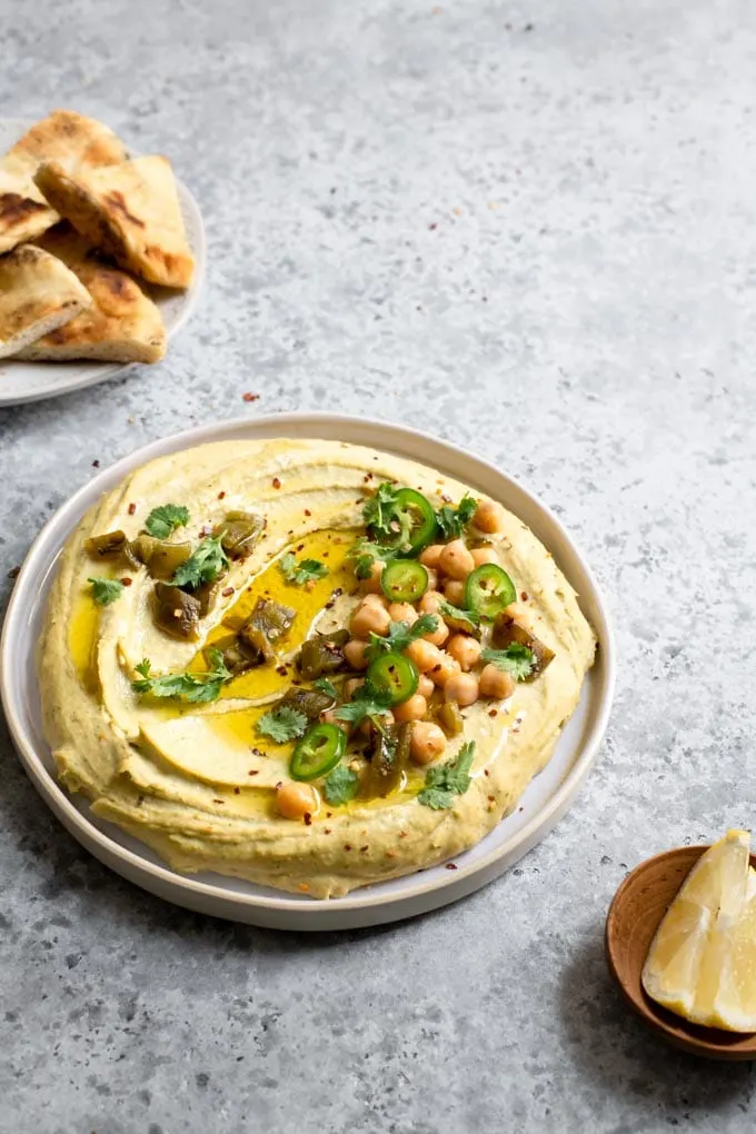 side view of roasted jalapeÃ±o and cilantro hummus topped with garnishes and extra virgin olive oil