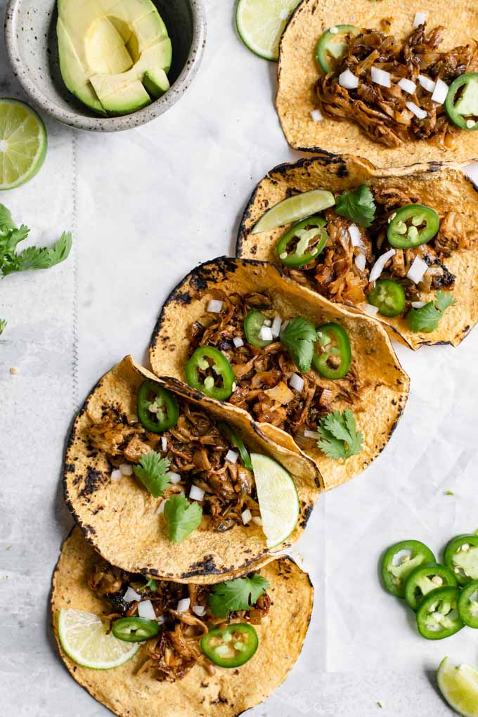 overhead view of 5 loaded carnitas tacos with a bowl of diced avocado on the side