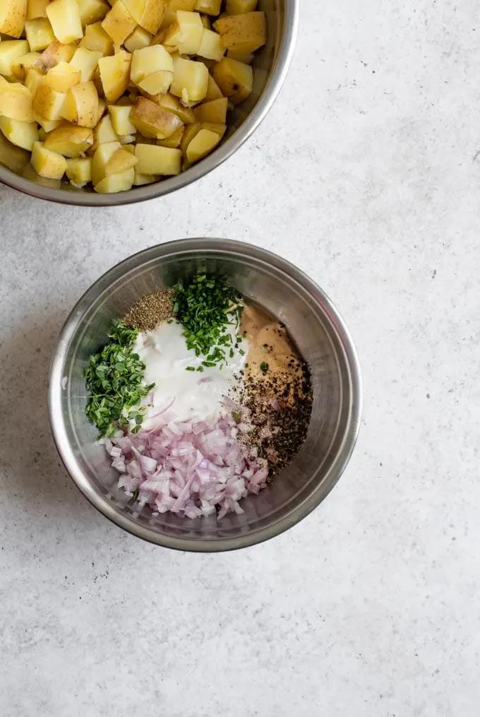 process shot showing the ingredients for the dressing for the potato salad in a bowl, with a second bowl in the edge of the photo showing the steamed potatoes