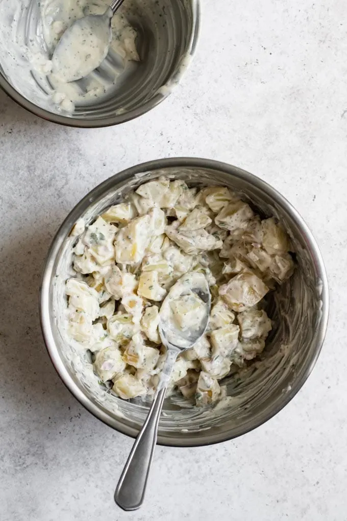 process shot showing the steamed potatoes tossed in herbed creamy vegan mayo dressing with the empty dressing bowl in the corner