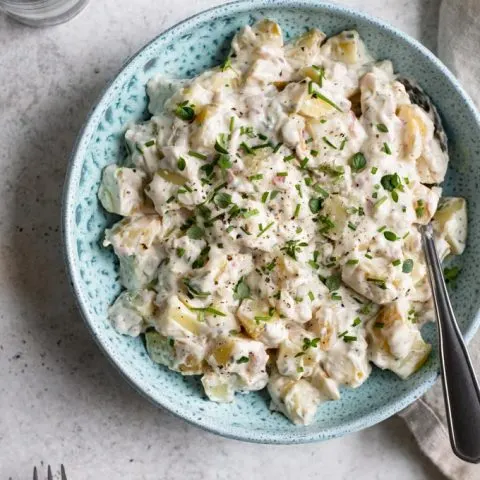 overhead view of vegan potato salad served in a blue bowl with plates on the edge of the photo for serving