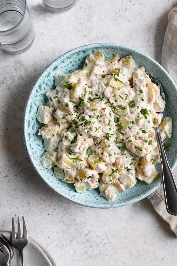 overhead view of vegan potato salad served in a blue bowl with plates on the edge of the photo for serving