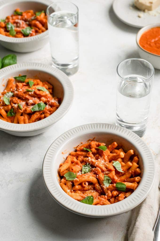 three bowls of pasta with vegan vodka sauce, topped with basil