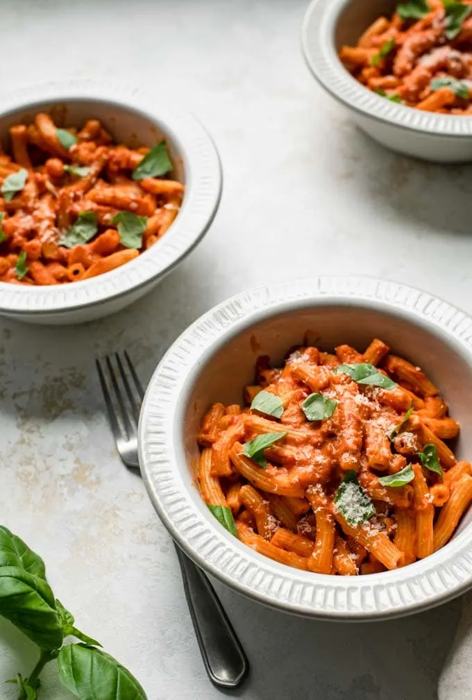 close up angled shot of three bowls filled with pasta with vegan vodka sauce,