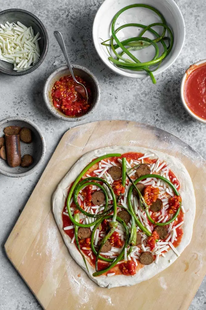 Garlic scape pizza assembled on the dough on a pizza peel before being baked