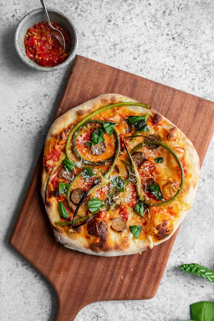 garlic scape pizza baked and on a cutting board with a bowl of calabrian chiles on the side