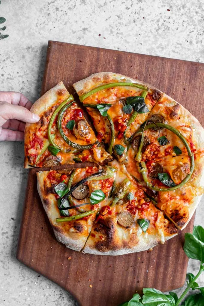 garlic scape pizza on a cutting board, sliced, with one slice being pulled to serve