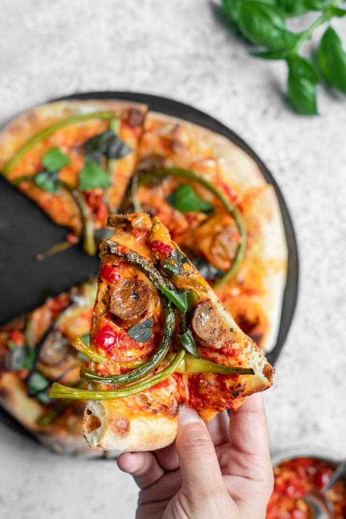 a slice of pizza held over the rest of the garlic scape pizza