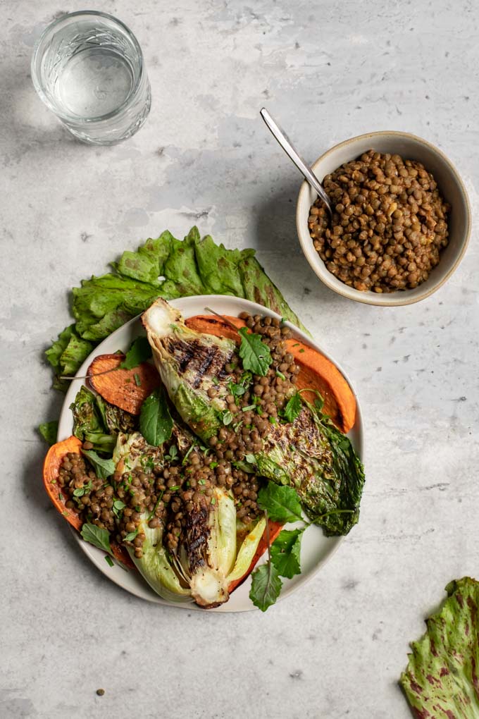 grilled salad with smoky lentils and sweet potato on a plate over a leaf of the radicchio, an bowl of lentils on the side