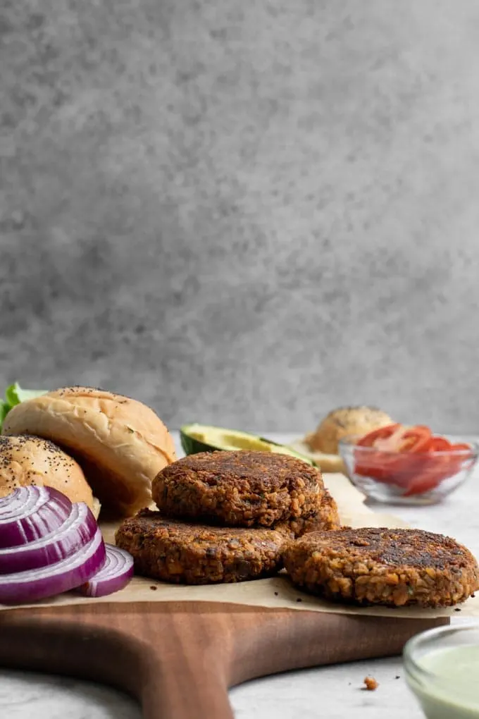 a side view of the veggie burgers cooked and ready to assemble with buns, sliced tomato, pesto cashew aioli, and red onion