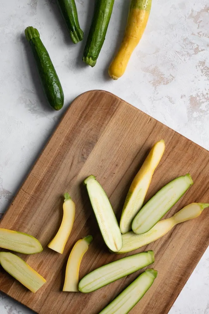 zucchini and yellow summer squash being cut in half on a cutting board