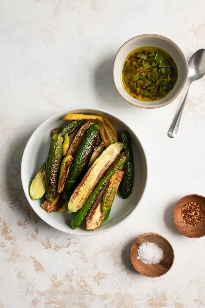 the pan fried squash in a large bowl, with the marinade mixed in a second bowl and flaked sea salt and red pepper flakes in pinch bowls