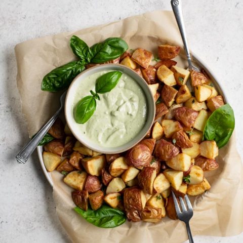 pesto cashew aioli in a bowl garnished with a sprig of basil served with roasted potatoes for dipping