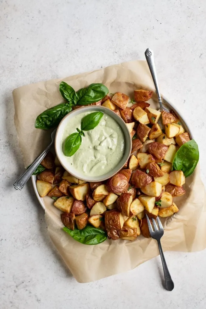 pesto cashew aioli in a bowl garnished with a sprig of basil served with roasted potatoes for dipping