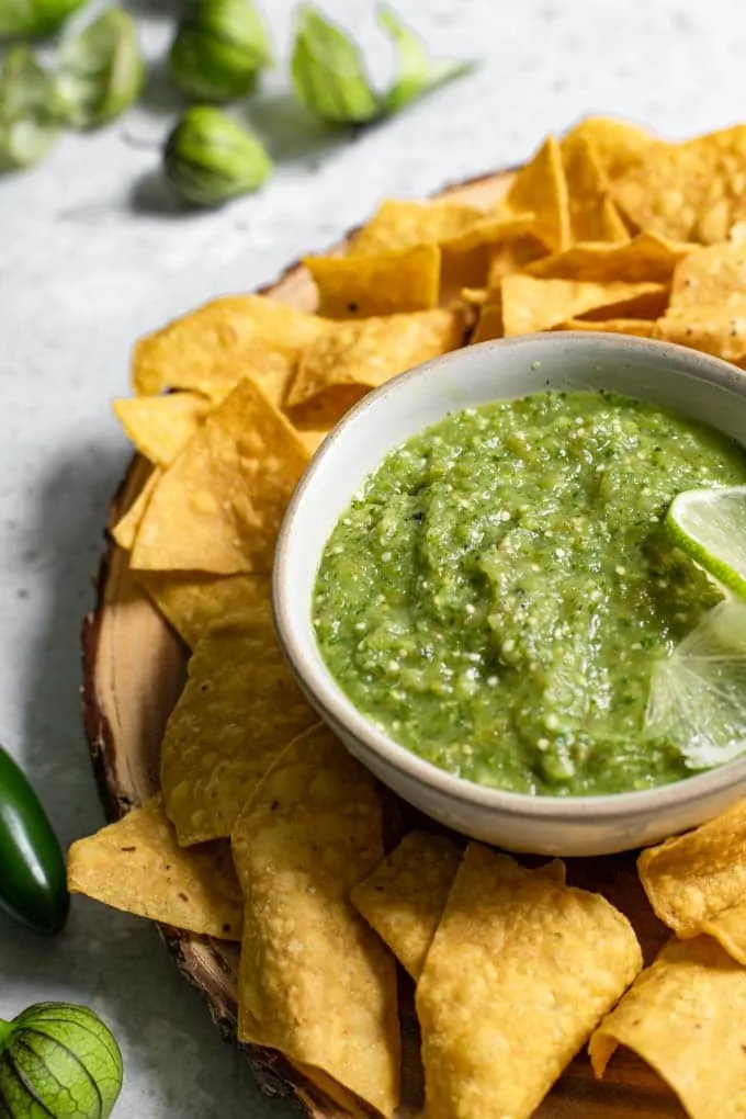 close up of the homemade tomatillo salsa served in a bowl with corn chips surrounding it