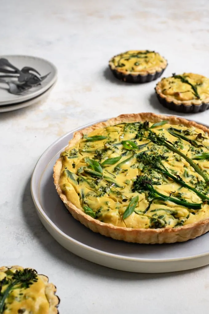the vegan sprouting broccoli quiche on a plate to serve, with the three mini quiches around it